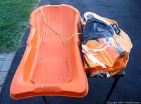 Top-down photo showing the orange plastic sled with rope and the folded double snow tube in a bag.