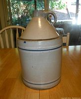 Full view of vintage stoneware jug with handle and blue stripes on a wooden table, lit by daylight from window