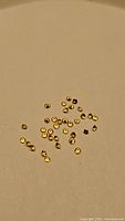 Photo showing a parcel of small round faceted golden yellow sapphires scattered on a beige surface.