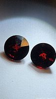 Pair of round, deep cherry red almandine garnet stones with faceted fancy cut under light showing their clarity and color.