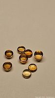 Photo of 8 round cabochon citrine gemstones laid on a white surface highlighting their golden yellow color and smooth polished surfaces with some visible inclusions.