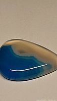 Close-up showing the pear-shaped blue striped agate cabochon with bright blue and cream color banding, polished surface reflecting light.