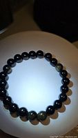 Front photo of natural golden sheen obsidian bead bracelet showing the evenly sized black beads with golden flashes and elastic string.