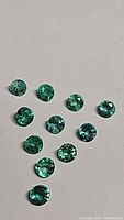 Top-down view of 13 round green faceted stones arranged in triangular formation