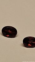 Close-up of two dark red oval cut garnet gemstones placed on a neutral background showing facets and reflections.