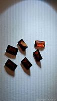 Six deep reddish-brown baguette cut garnet stones arranged on white background, showing clarity and color