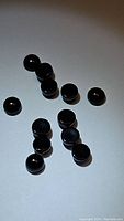 Top view showing 14 small round polished black onyx cabochon gemstones scattered on a white surface, each approximately 4mm diameter.