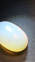 Close-up image of a polished oval cabochon cut opal gemstone with visible rainbow color play.