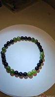 Stretch bracelet with alternating polished round 6mm beads of green jade and black onyx placed on a white surface.