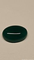 Photo of natural green onyx oval cabochon gemstone lying flat on surface under neutral lighting showing smooth polished surface and rich green color.