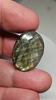 Photo of natural labradorite gemstone held between fingers showing front view with golden yellow flashes and checkerboard cut facets.