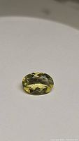 Photo of oval cut lemon citrine gemstone with clear yellow-green color and visible facets on white background.