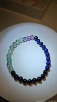 Natural Mix Gemstone Stretchy Bracelet laid flat showing distinct bead sections of blue Lapis Lazuli, green Fluorite, and black Onyx under bright light.