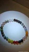 Circular, stretchy bracelet made up of polished mixed gemstone beads of various colors including green, white, black, pink, yellow, red, and purple.
