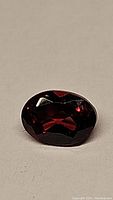 Close-up photo of oval cut deep cherry red garnet gemstone from Mozambique on a surface showing faceted cuts and color.