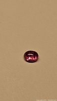 Oval cabochon natural pink sapphire on a beige background, showing overall color and shape.