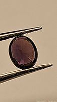Close-up image of a natural purple sapphire held by tweezers showing its oval cut and faceting details.