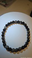 Front view showing the round polished beads of the natural silver sheen obsidian bracelet laid flat in a circular shape.