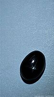 Oval cabochon cut dark star diopside gemstone showing the 4-ray star asterism effect under light.