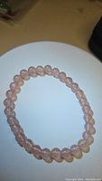 Photo showing a round stretchy bracelet made of translucent pink natural strawberry quartz beads, laid flat on a white surface under ambient light.
