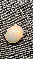 Natural untreated Ethiopian opal cabochon 9x7mm showing rolling rainbow color flashes on a textured black background.