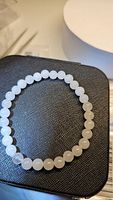 Close-up of natural white jade bead bracelet arranged in a circular shape on textured surface, showing bead uniformity and translucence.