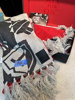 Two scarfs, one black and white geometric pattern with 2021 tag and one solid red, both new in box, displayed with their packaging.