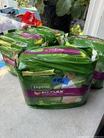 Photo showing multiple green packs of Depend Fit-Flex XL incontinence underwear with purple label, each containing 15 pieces, stacked on a table.