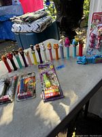 Wide view of 20 PEZ dispensers on table showing variety of character heads and two sealed Jurassic World dispensers