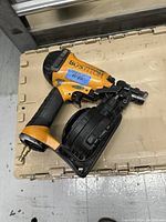 Yellow and black Bostitch air nailer laying on a beige surface with visible wear and a blue tape label marked '#13'.