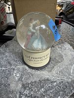 Photo of the Cinderella snow globe featuring Cinderella and Prince Charming inside the clear globe with base reading 'A Perfect Fit right from the start Cinderella'. Globe rests on bubble wrap.