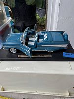 Blue die cast model of 1957 Chevy Bel Air convertible showing side profile with open doors and striped seats.