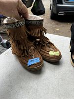 Top and side view of the pair of brown suede ladies moccasin boots with fringe and decorative beaded trim held upright