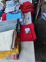Photo showing various folded towels including red towel with elephant embroidery, blue, red, white, cream, yellow patterned, and multicolor striped towels.