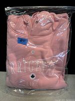 Pink hoodie with white print folded and sealed in clear plastic bag. Blue sticker with #50 affixed on the bag.