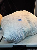 White queen size down comforter folded and sitting on a table, showing wrinkles and some stains.