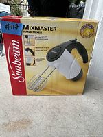 Front and side view of the Sunbeam Mixmaster hand mixer box showing product image, brand, and features.