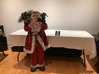 Full view of the Santa Claus statue standing around 4 feet tall in red fur-trimmed suit holding bag of gifts and garland