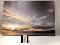 Full front view of canvas wall art showing the sunset over water and land with dramatic clouds.