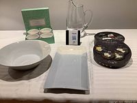 Large clear glass water decanter, Sophie Conrad white porcelain ramekins in box, four round cheese plates in packaging, Royal Doulton two-tone rectangular platter, large white bowl on table