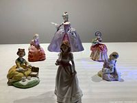 Seven hand-painted porcelain figurines arranged on flat surface showcasing various poses and detailed colorful dresses.
