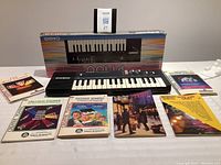 Casio PT-100 keyboard with original box and instructional books spread out on table.