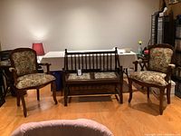 Full view of the three-piece set placed on wooden flooring against a plain wall, featuring two armchairs and a two-seat bench with floral cushions.