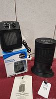 Photo showing both heaters, the black ceramic heater on its box and the black tower heater with control buttons on top, along with an instruction manual and auction clip.