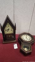 Both vintage clocks shown side by side on red cloth background