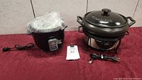 Both Crock Pot and rice cooker with power cords displayed on red cloth surface.