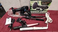 Conair 1875 blowdryer with diffuser, three curling irons on red cloth surface with box behind