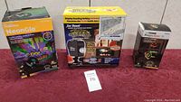 Front view showing three boxed outdoor projection lights from different brands including NeonGlo Halloween, Star Shower Window Wonderland, and an unnamed Halloween projector.