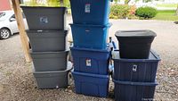 Large pile of various storage totes in gray, blue, and black, stacked in three columns outdoors.