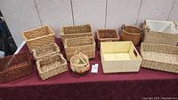 Multiple wicker baskets and trays arranged on a burgundy cloth-covered table.